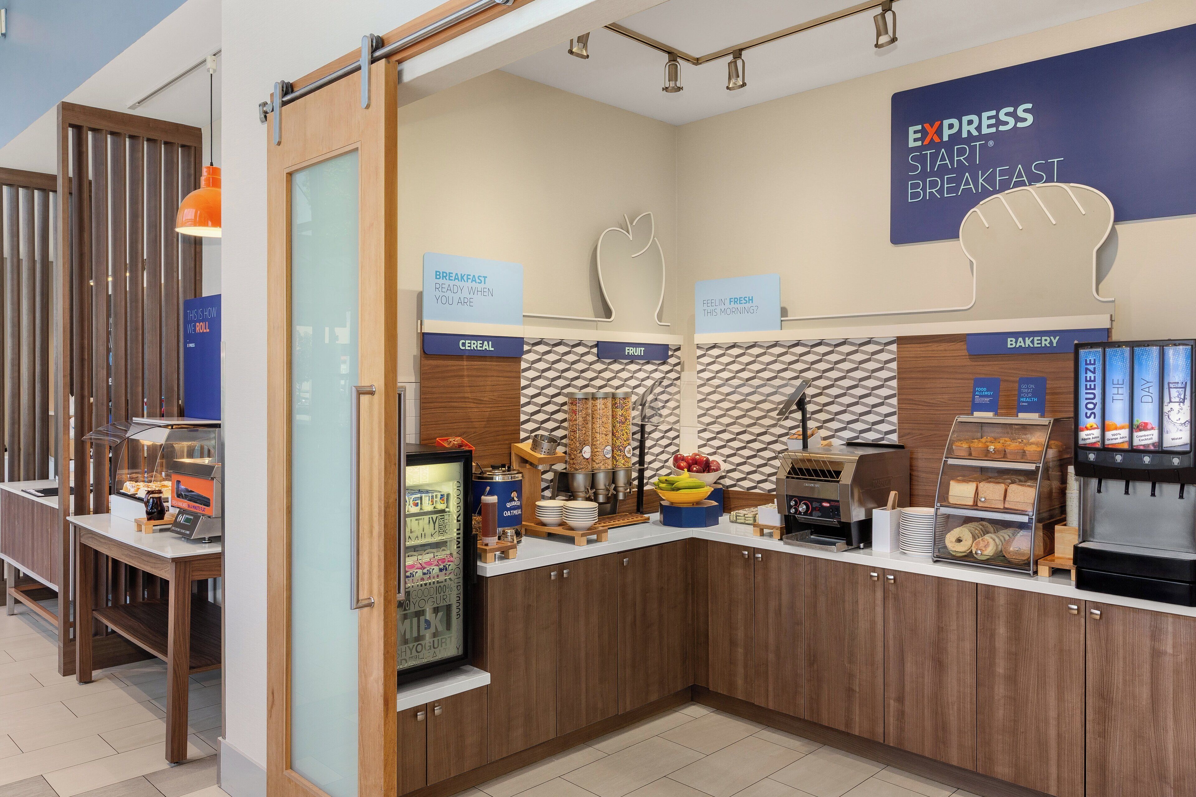 A breakfast area with a sign indicating it's ready when you are, cereal, fruit, and a bakery section.
