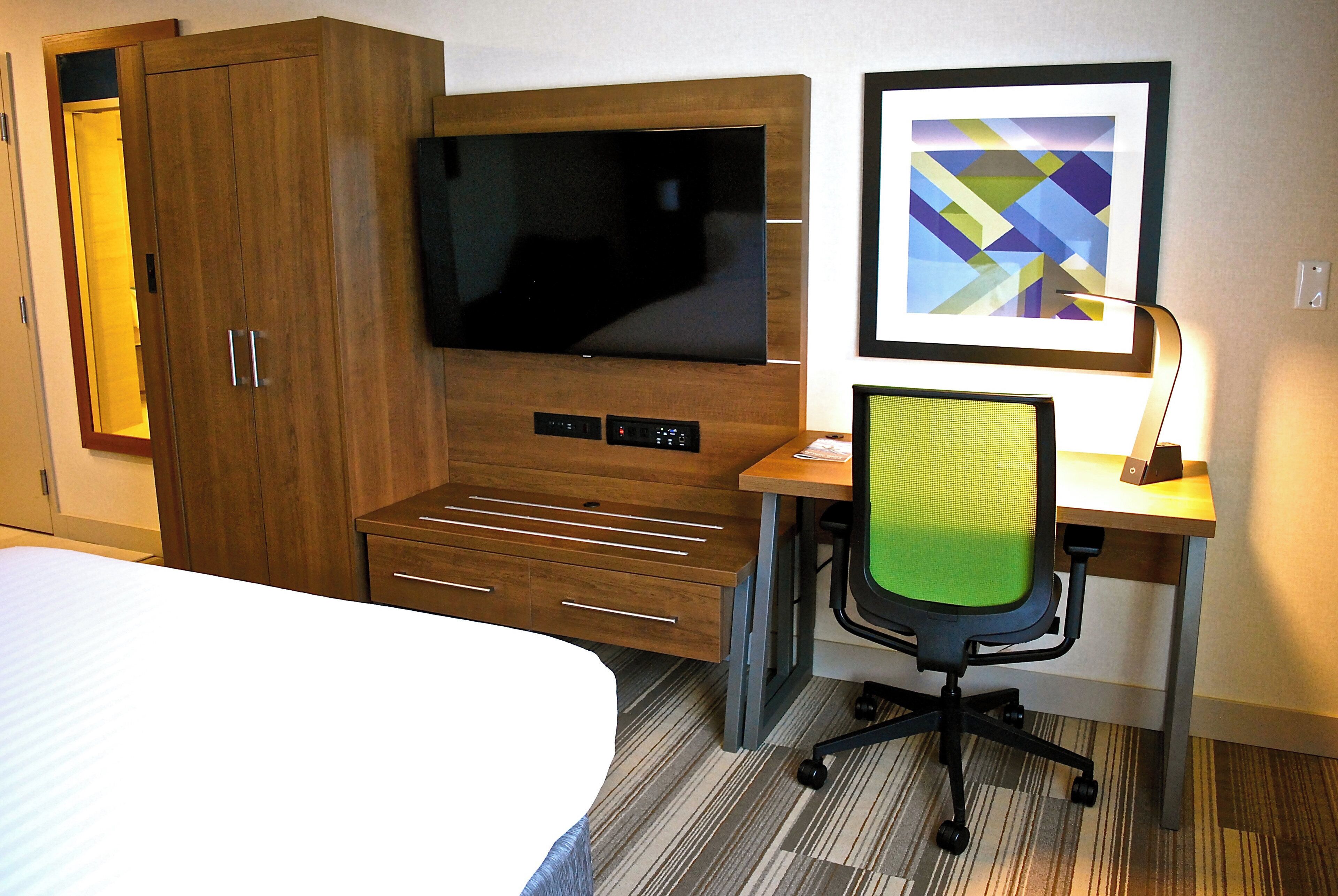 Habitación de hotel con una cama, un escritorio con silla, un televisor y una obra de arte enmarcada en la pared.