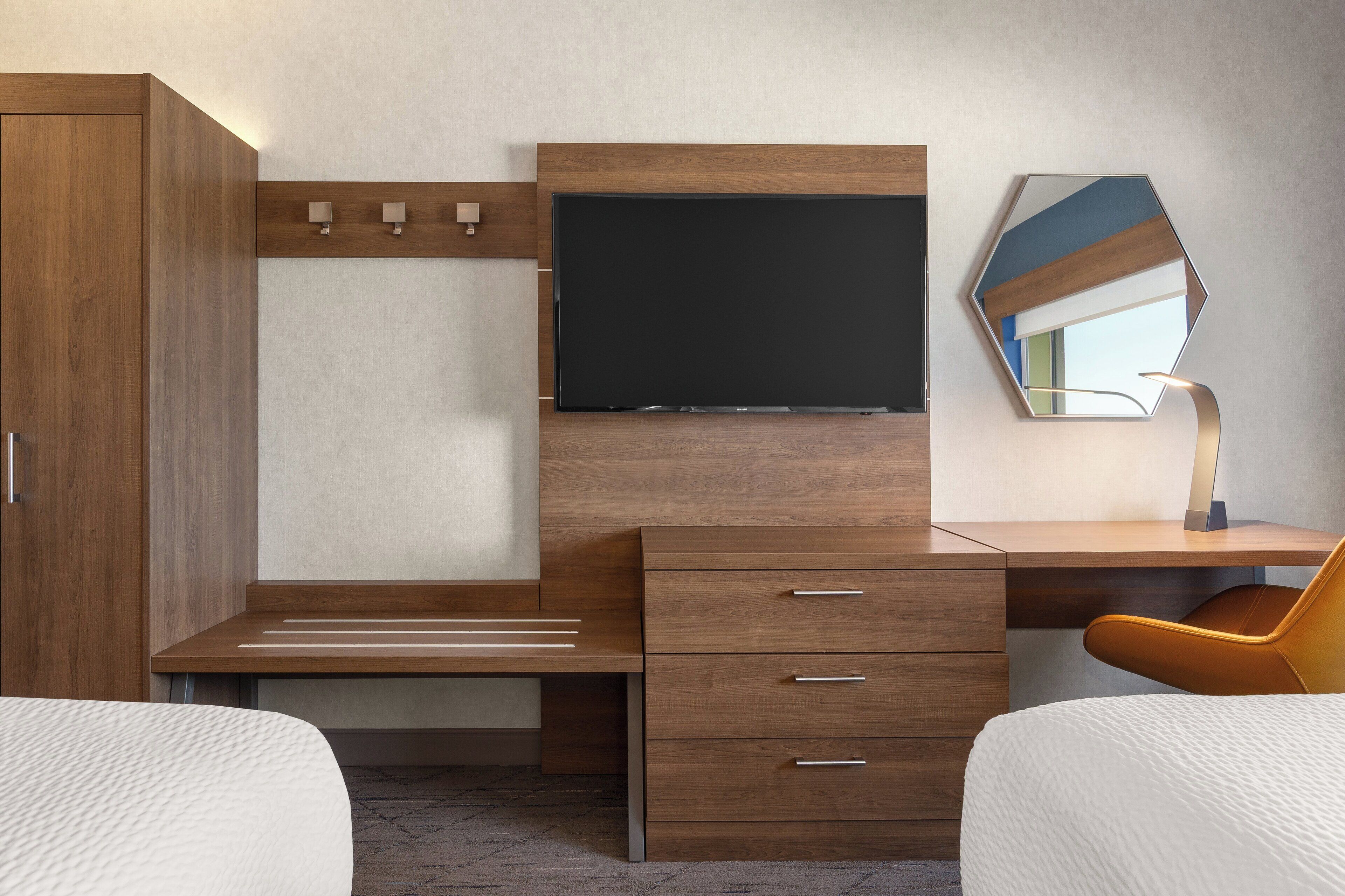 Una habitación de hotel moderna con un escritorio de madera, un televisor de pantalla plana, un espejo y una cama.