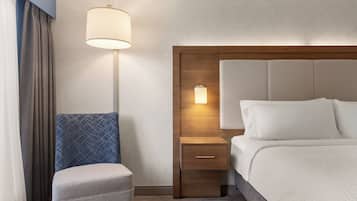 Une chambre d’hôtel avec un lit, une table de chevet avec une lampe, une chaise et une tête de lit en bois.