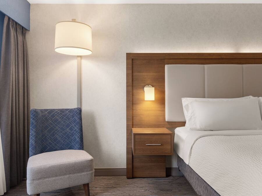 Une chambre d’hôtel avec un lit, une table de chevet avec une lampe, une chaise et une tête de lit en bois.