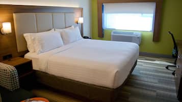 A hotel room with a large bed, bedside lamps, a window with an air conditioner, and a small table with a magazine.