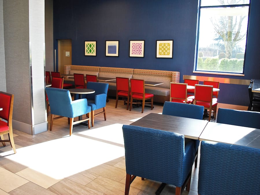 A restaurant with booths and tables, red and blue chairs, and framed artwork on the wall.