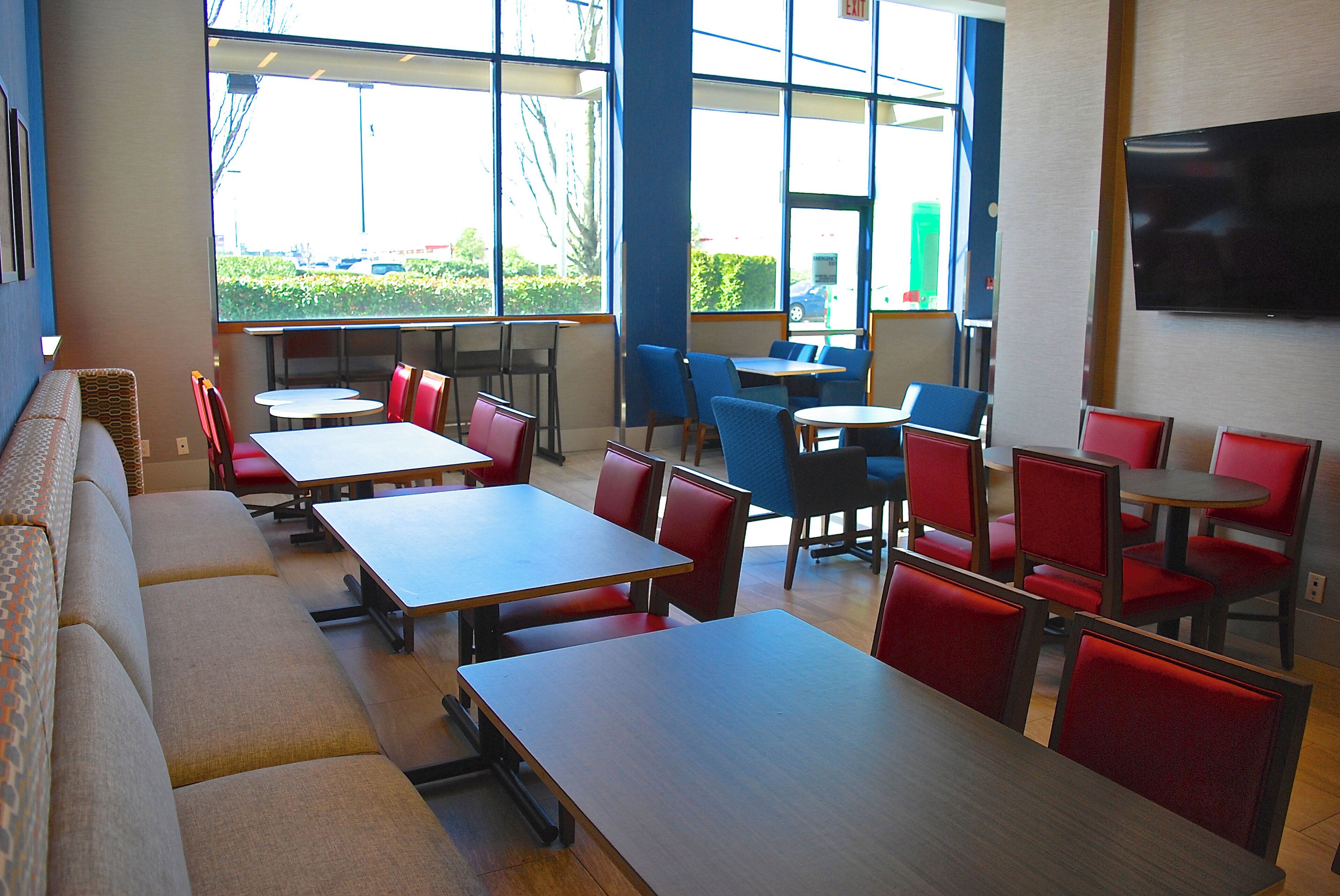 A dining area with tables and chairs, large windows, and a flat-screen TV on the wall.