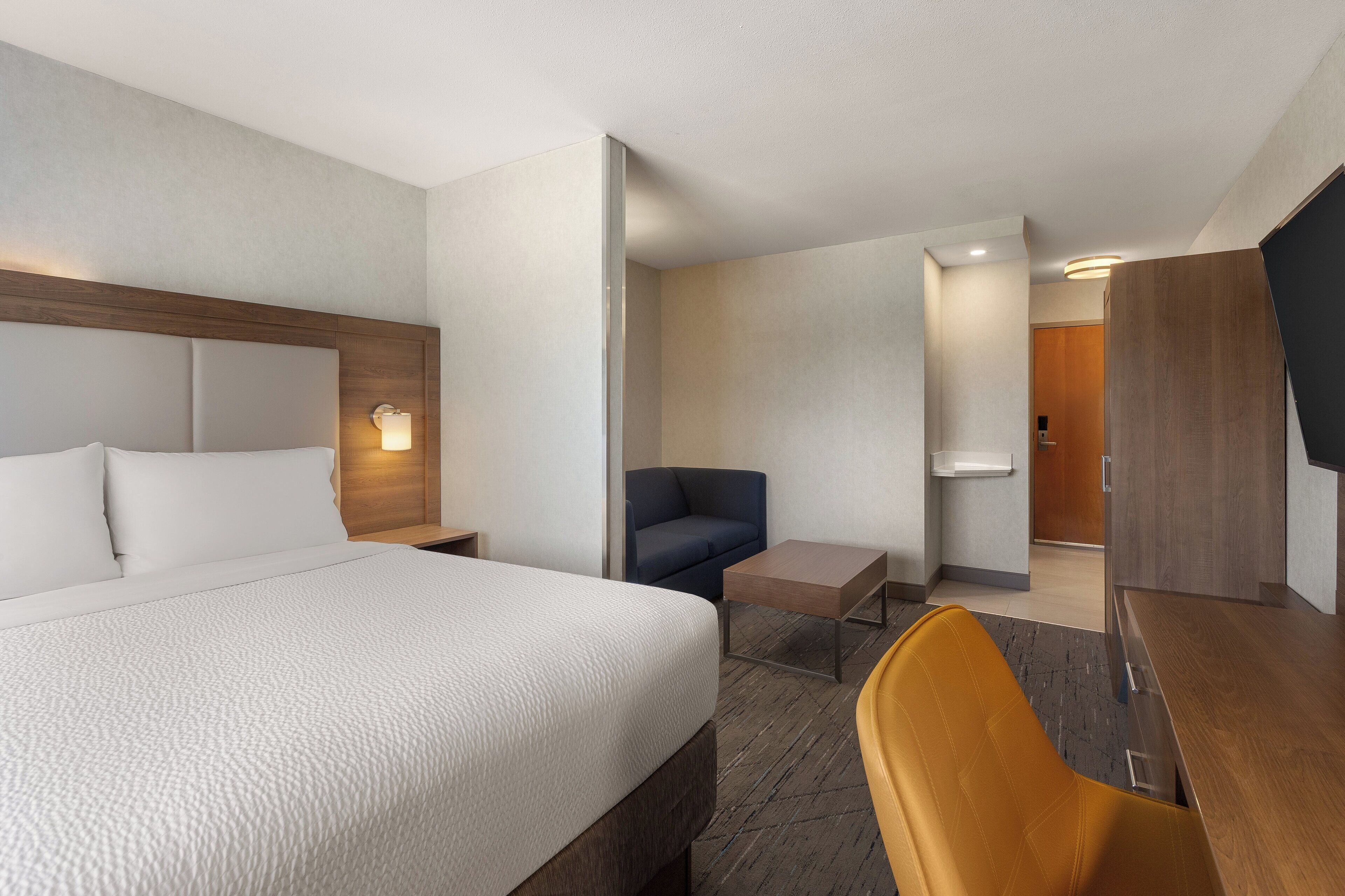 A hotel room with a large bed, a desk, a chair, a sofa, and a television.