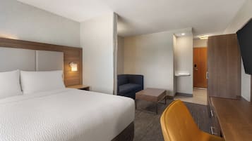 A hotel room with a large bed, a desk, a chair, a sofa, and a television.