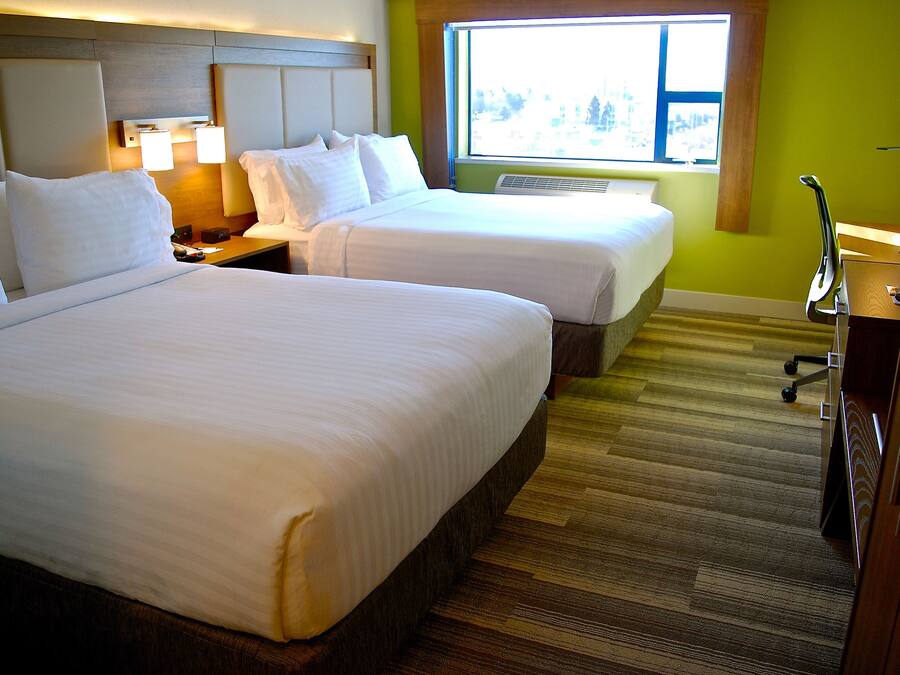 A hotel room with two beds, a desk, a chair, and a window with a view.