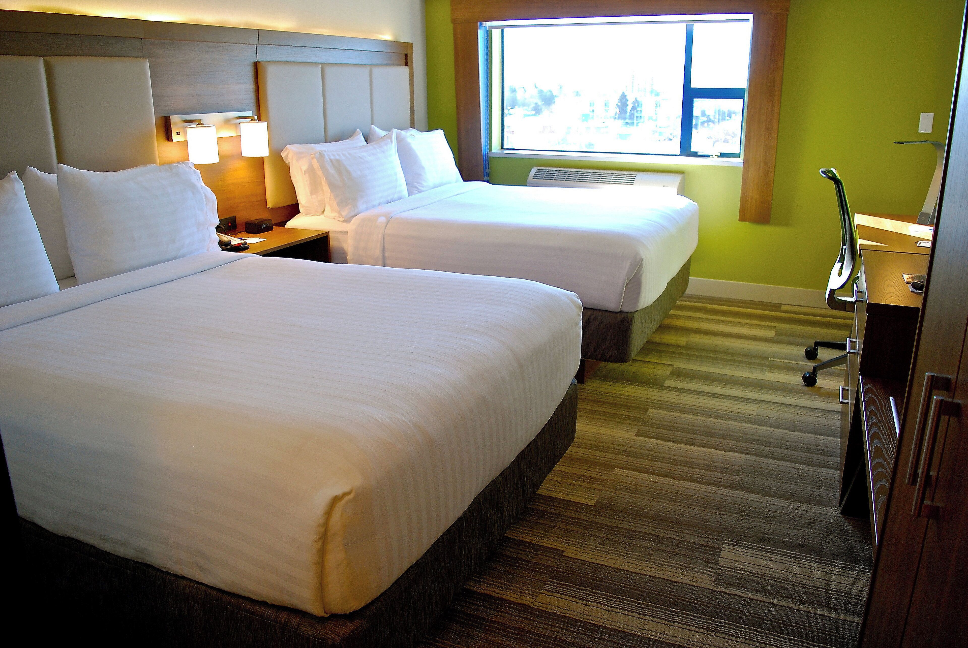 A hotel room with two beds, a nightstand, a lamp, a desk, and a window with a view.