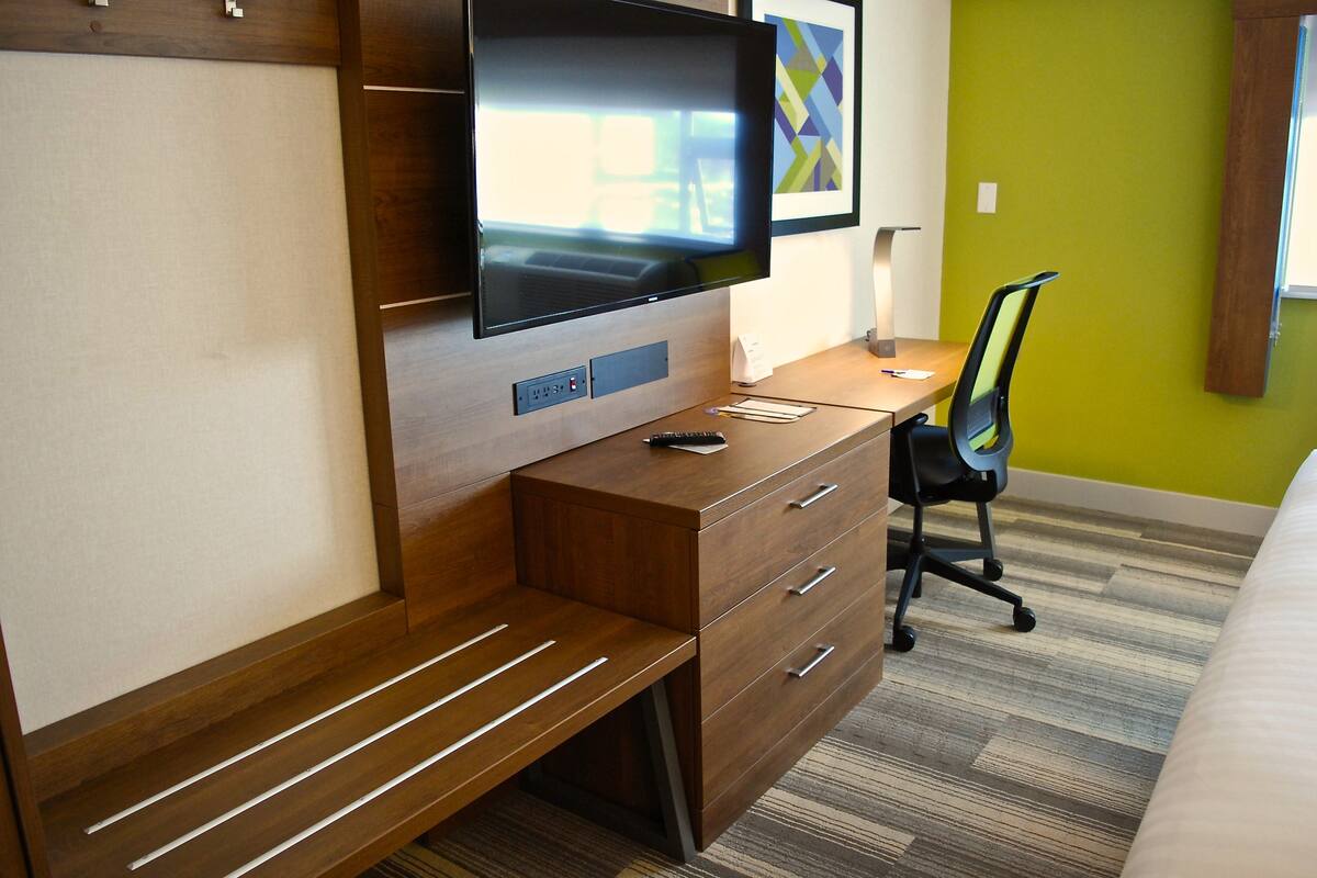 Une chambre d’hôtel avec un bureau en bois, un téléviseur à écran plat fixé au mur, une chaise et un lit.