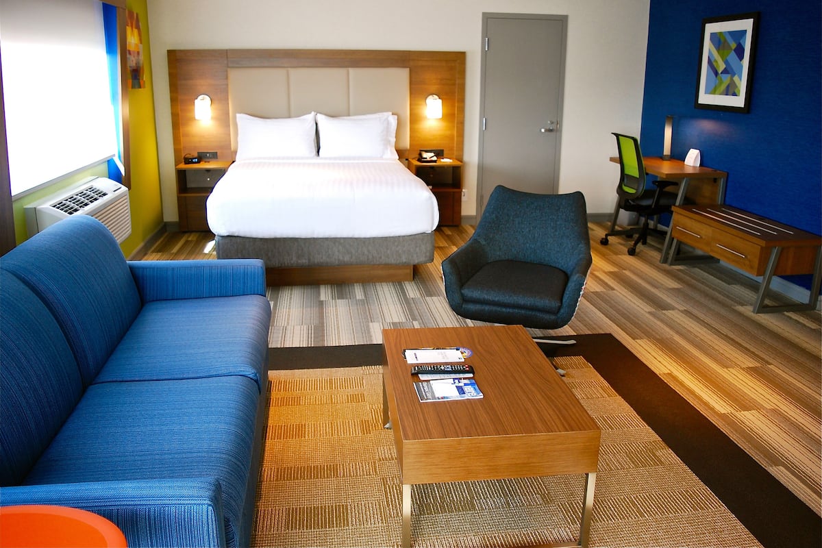 Une chambre d’hôtel avec un lit, un canapé bleu, une table basse en bois et un bureau avec une chaise.
