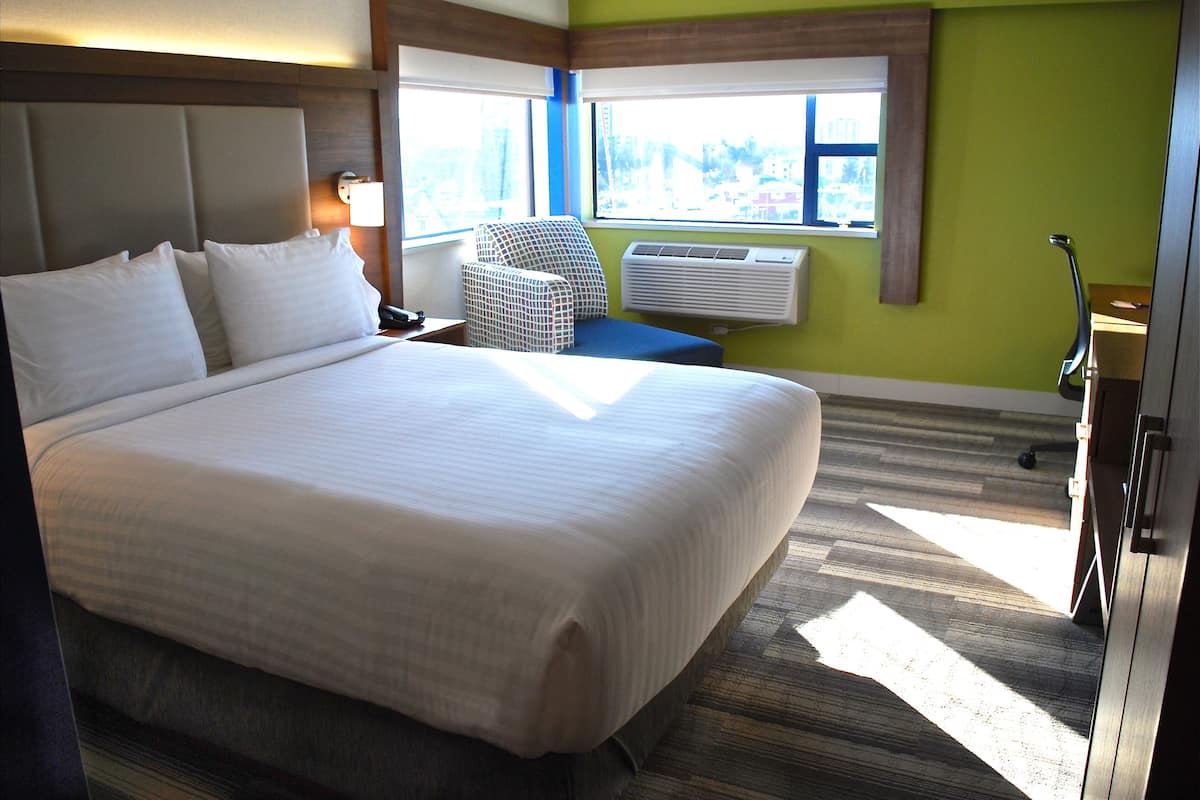 Une chambre d’hôtel avec un grand lit, une chaise, un appareil de climatisation et une fenêtre donnant sur un beau paysage.