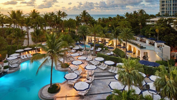 Un resort con piscina, sillas de descanso, sombrillas y palmeras.