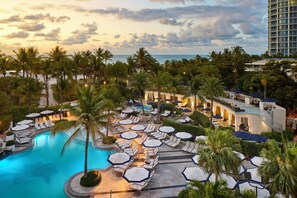 Un resort con piscina, sillas de descanso, sombrillas y palmeras.