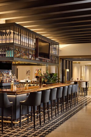 A bar area with a long counter, multiple stools, and a variety of bottles.