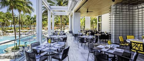 A restaurant with outdoor seating overlooking a pool, featuring a modern design with white pillars and black chairs.