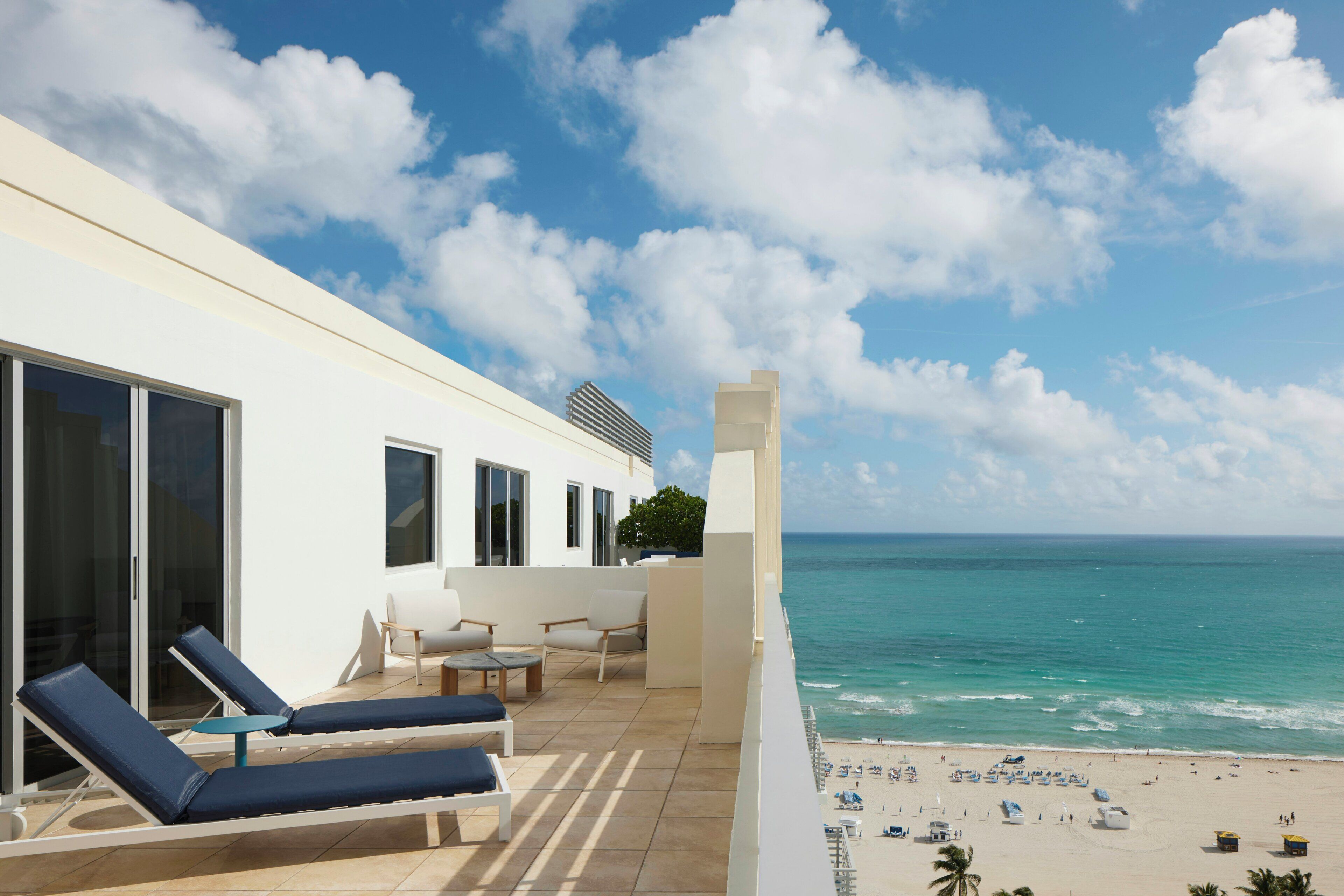 Un balcón moderno en un hotel con sillones de sol, mesa de billar y vistas al océano y la playa.