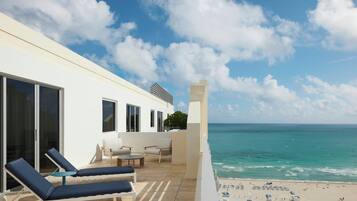 Un balcón moderno en un hotel con sillones de sol, mesa de billar y vistas al océano y la playa.