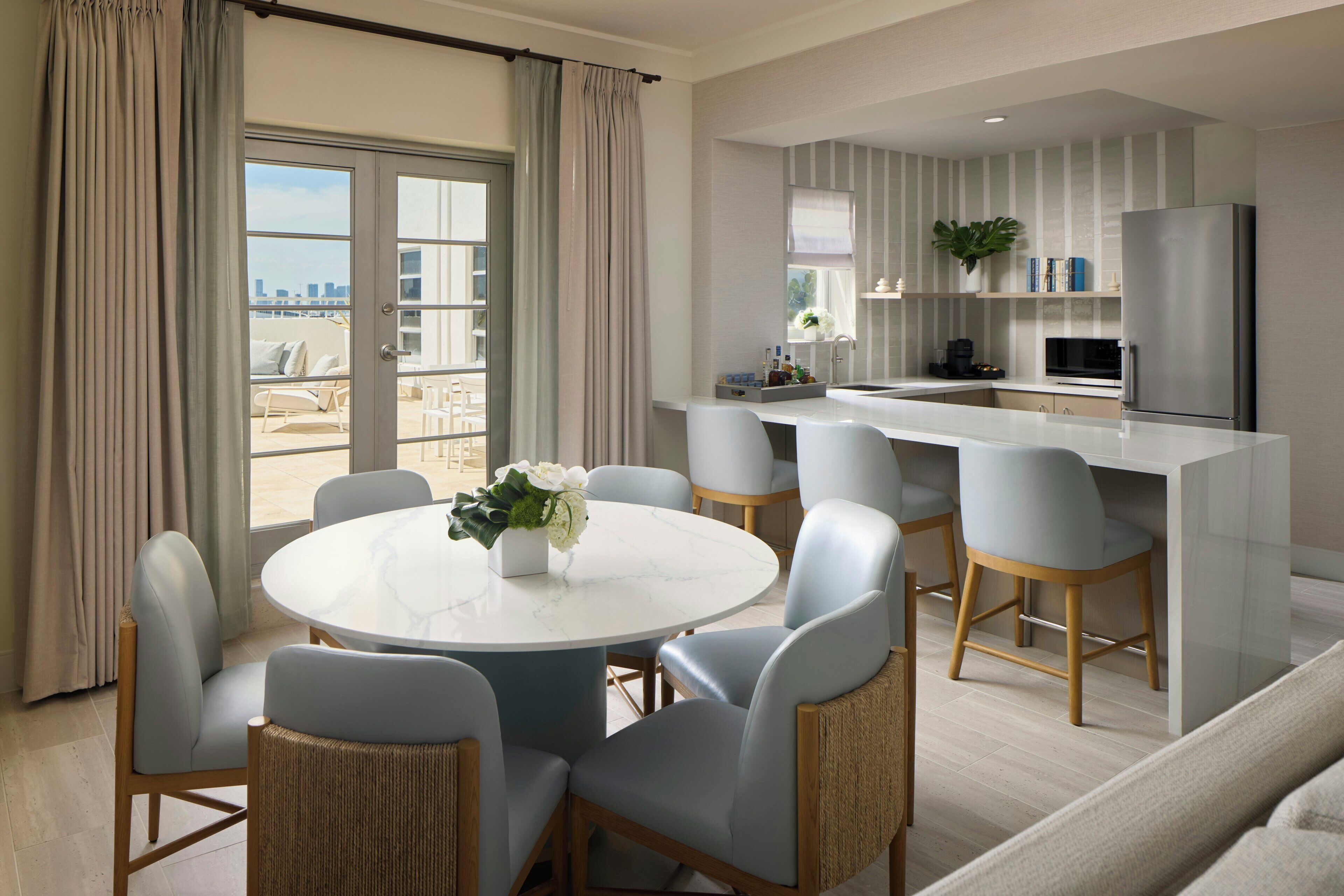 Una cocina moderna con una isla central, un comedor con una mesa redonda y sillas, y vistas de la ciudad a través de amplias ventanas.