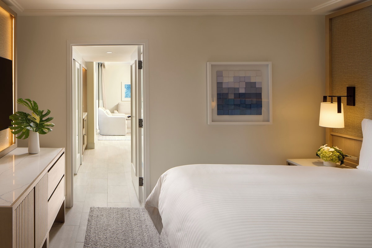 Una habitación de hotel con cama, mesita de noche, lámpara y una planta en maceta.