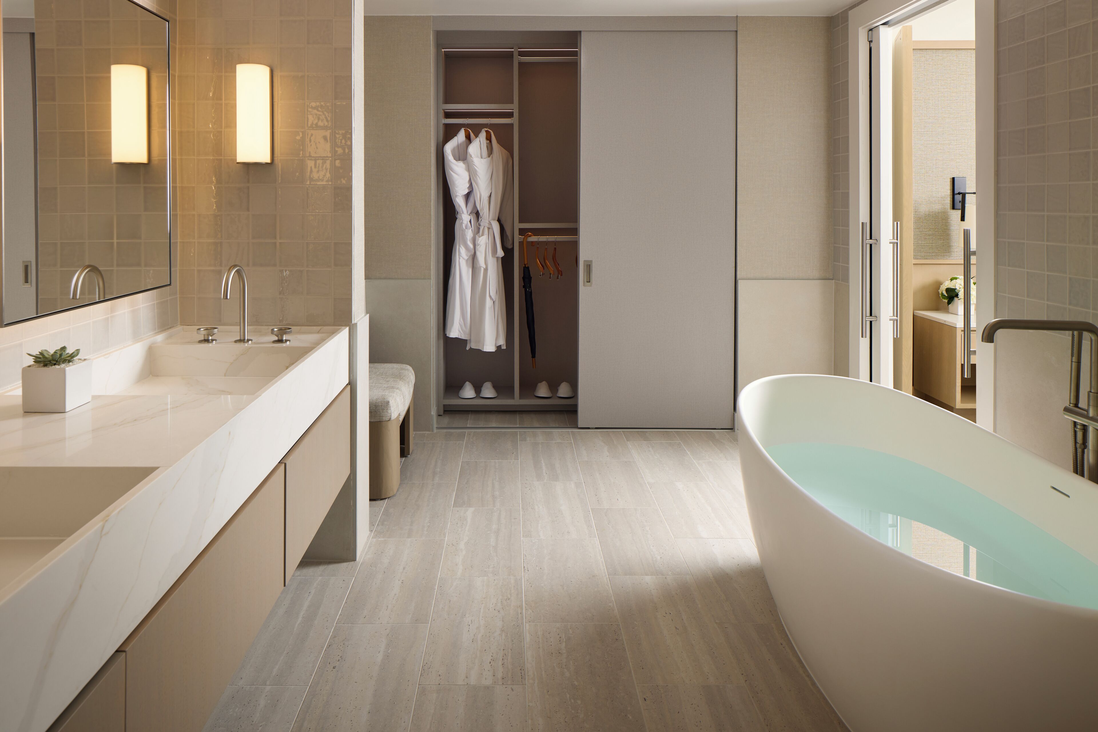 A modern bathroom with a freestanding bathtub, a large mirror, and a walk-in closet with hanging robes.