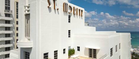 A white building with 'St. Moritz' on the facade, a rooftop patio with outdoor furniture, and a view of the ocean.