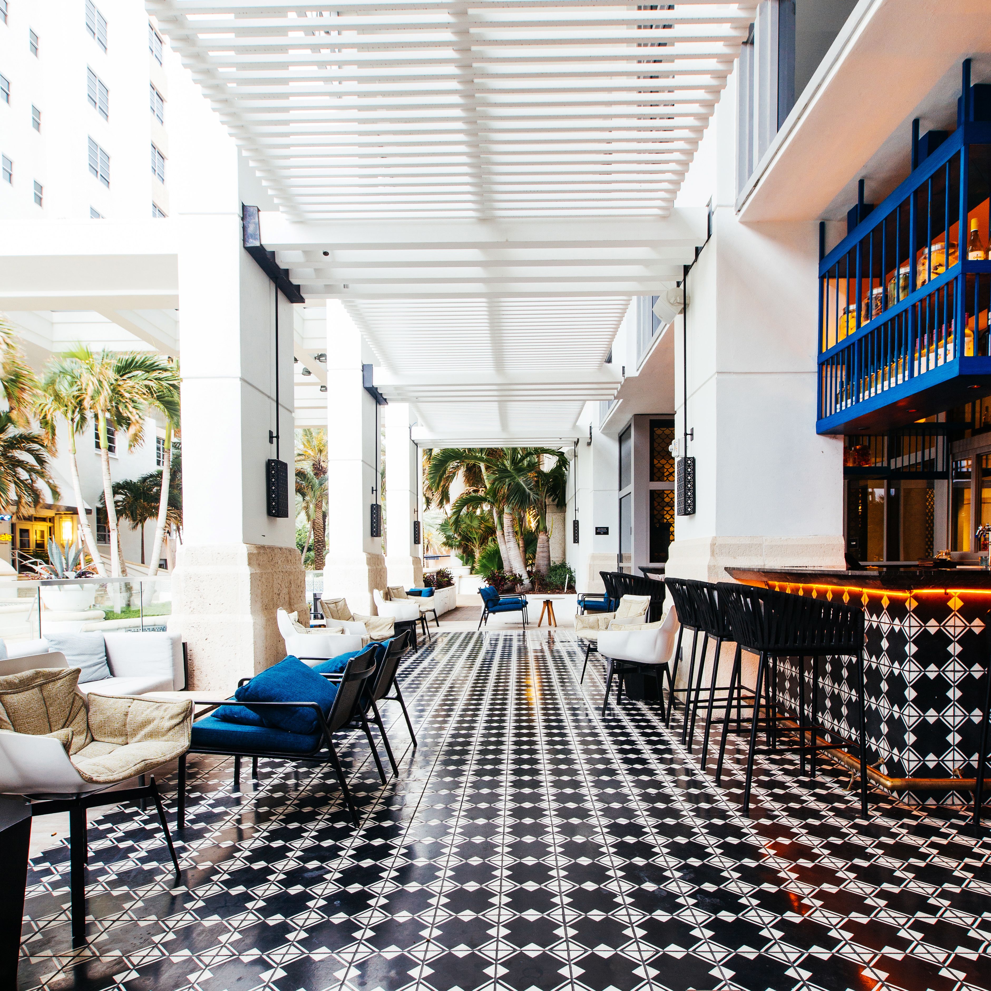 A covered outdoor seating area with a patterned floor, white and blue furniture, and a bar with blue shelves.