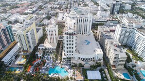 An aerial view of a hotel with multiple high-rise buildings, a rooftop pool, and surrounding greenery.
