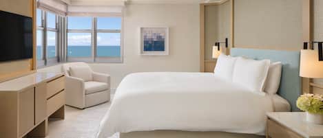 A modern hotel room with a large bed, a desk, a chair, and a television.