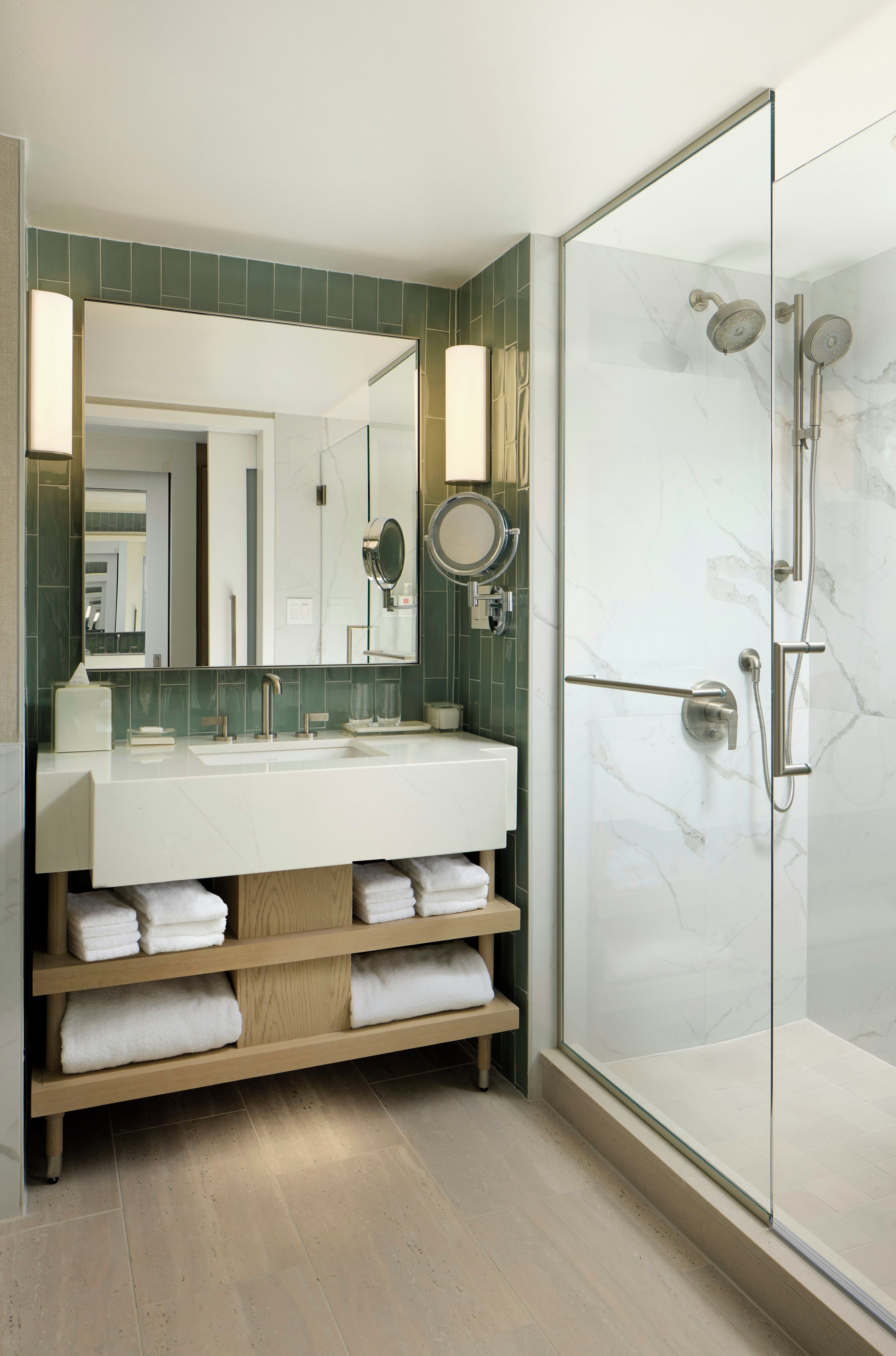 A modern bathroom with a glass-enclosed shower, a large mirror, and a vanity with a marble countertop.