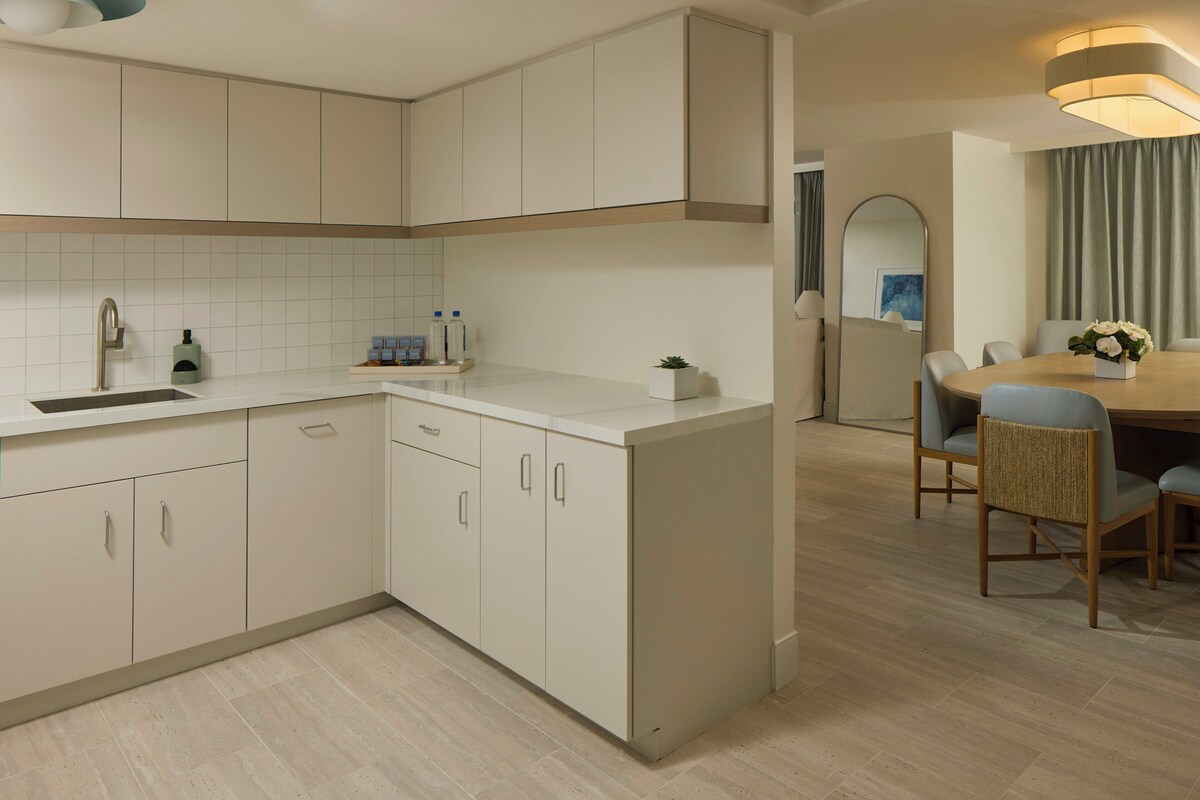 Una cocina moderna con armarios blancos, una encimera y un comedor con mesa y sillas.