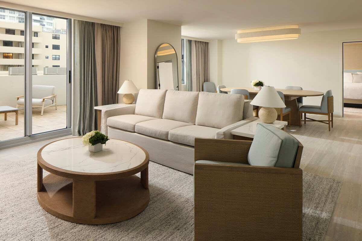 A modern hotel room with a sofa, armchairs, a dining table, and a round coffee table.