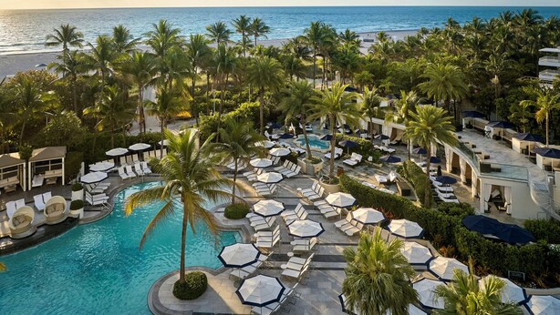 Un complexe hôtelier doté d’une piscine, de chaises longues, de parasols et de palmiers.
