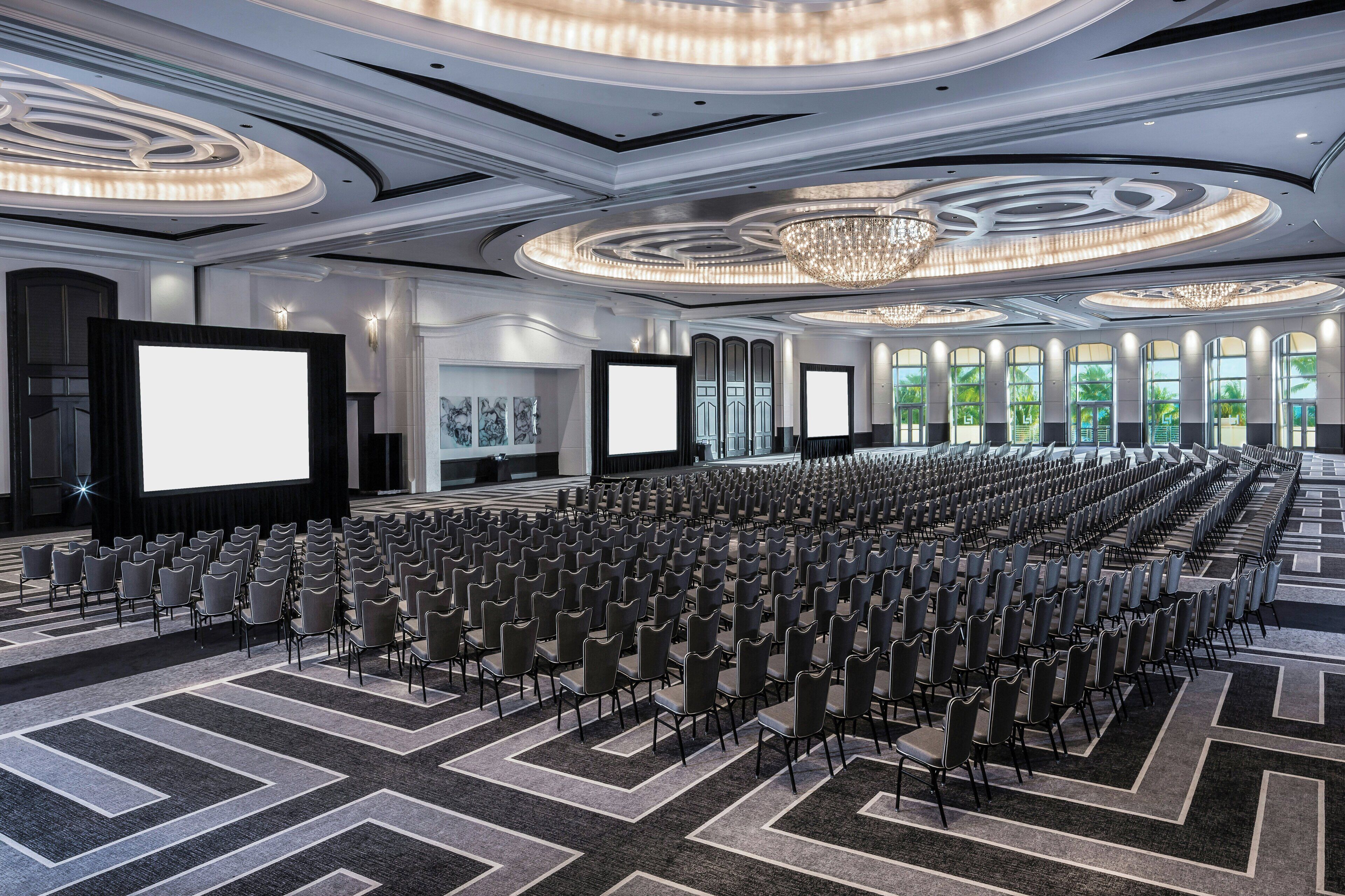 A conference room with rows of chairs, large screens, and a chandelier.