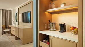 A modern hotel room with a wooden desk, a coffee machine, and a fruit basket.