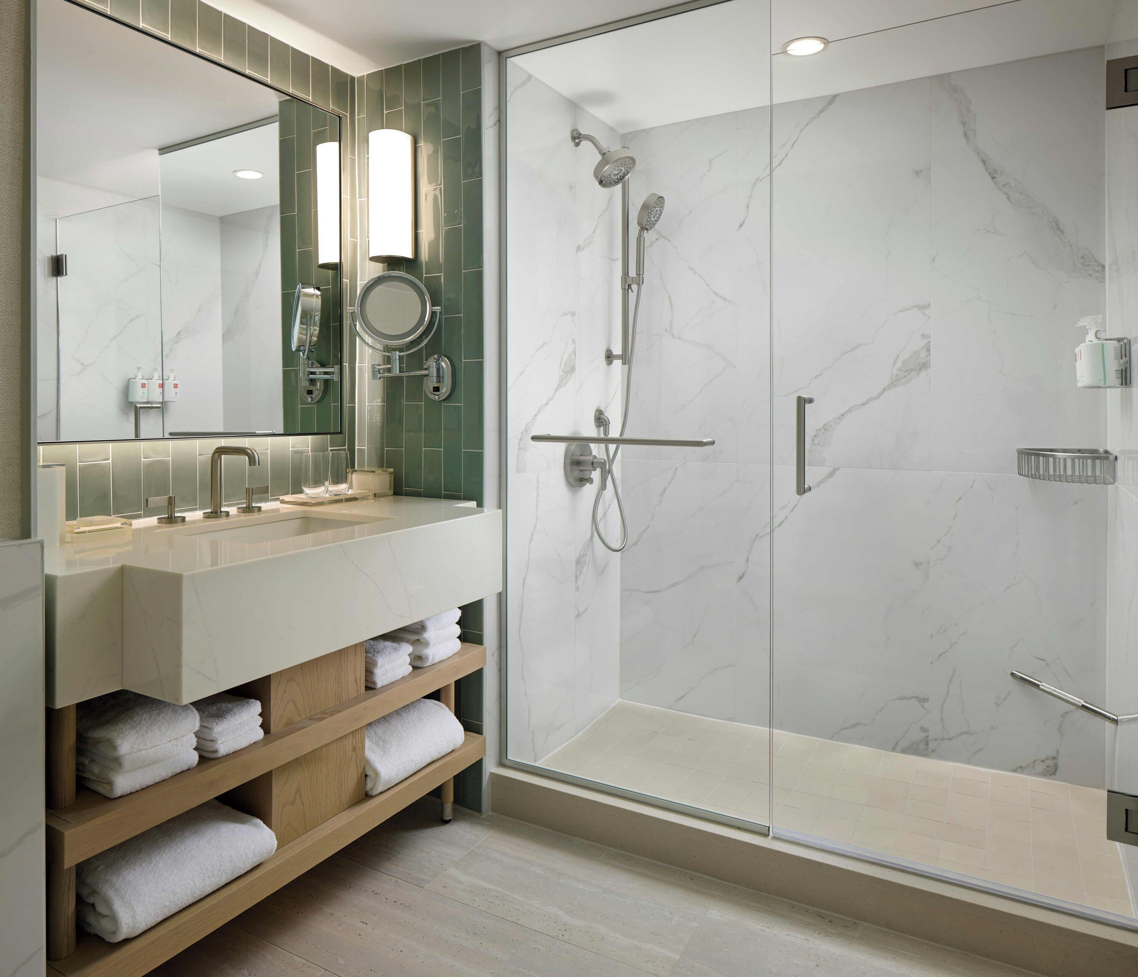 A modern bathroom with a glass-enclosed shower, a vanity with a mirror, and shelves with folded towels.