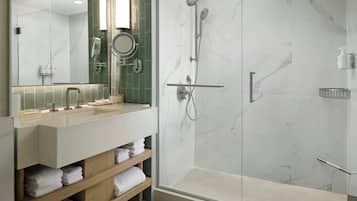 A modern bathroom with a glass-enclosed shower, a vanity with a mirror, and shelves with folded towels.