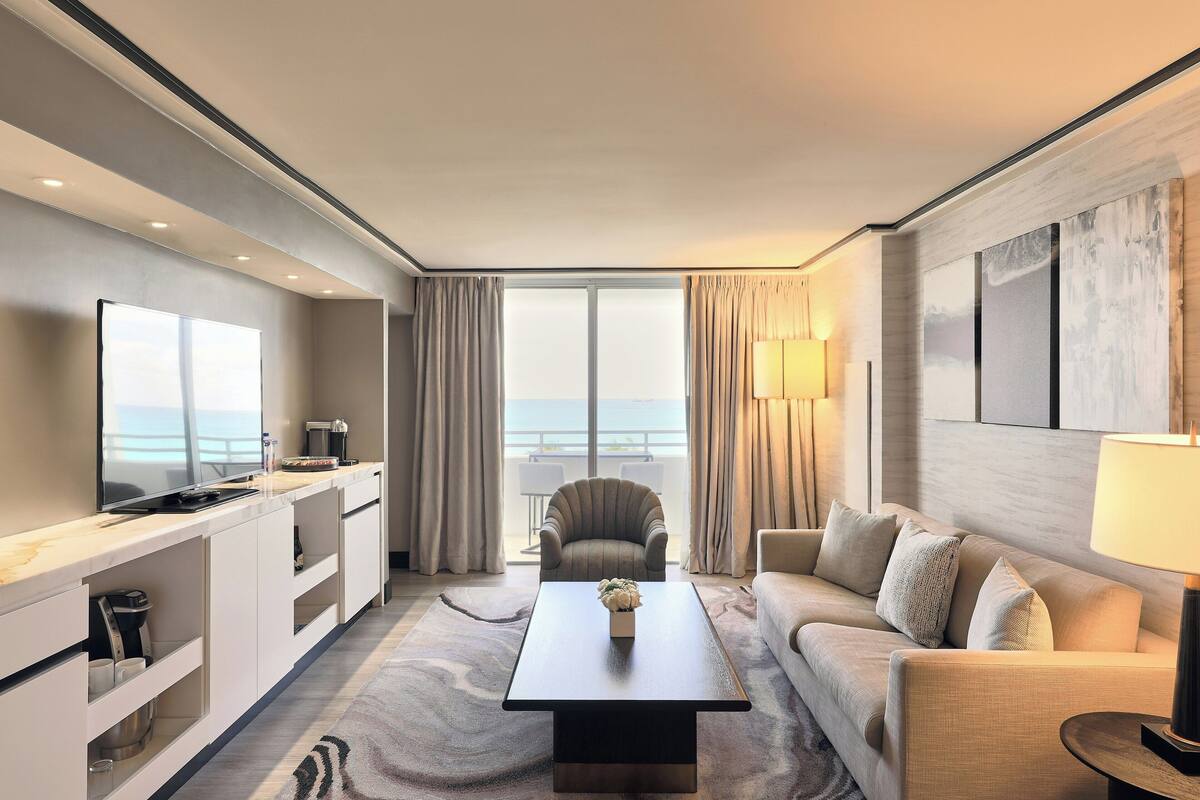 Une chambre d’hôtel moderne dotée d’une télévision à écran plat, d’un canapé, d’une table basse et offrant une vue sur la mer.