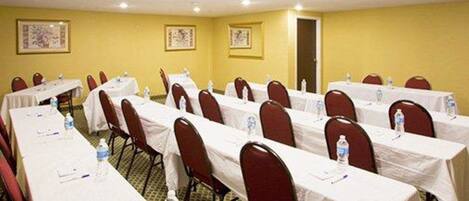A conference room with multiple tables and chairs, water bottles on each table, and framed pictures on the walls.