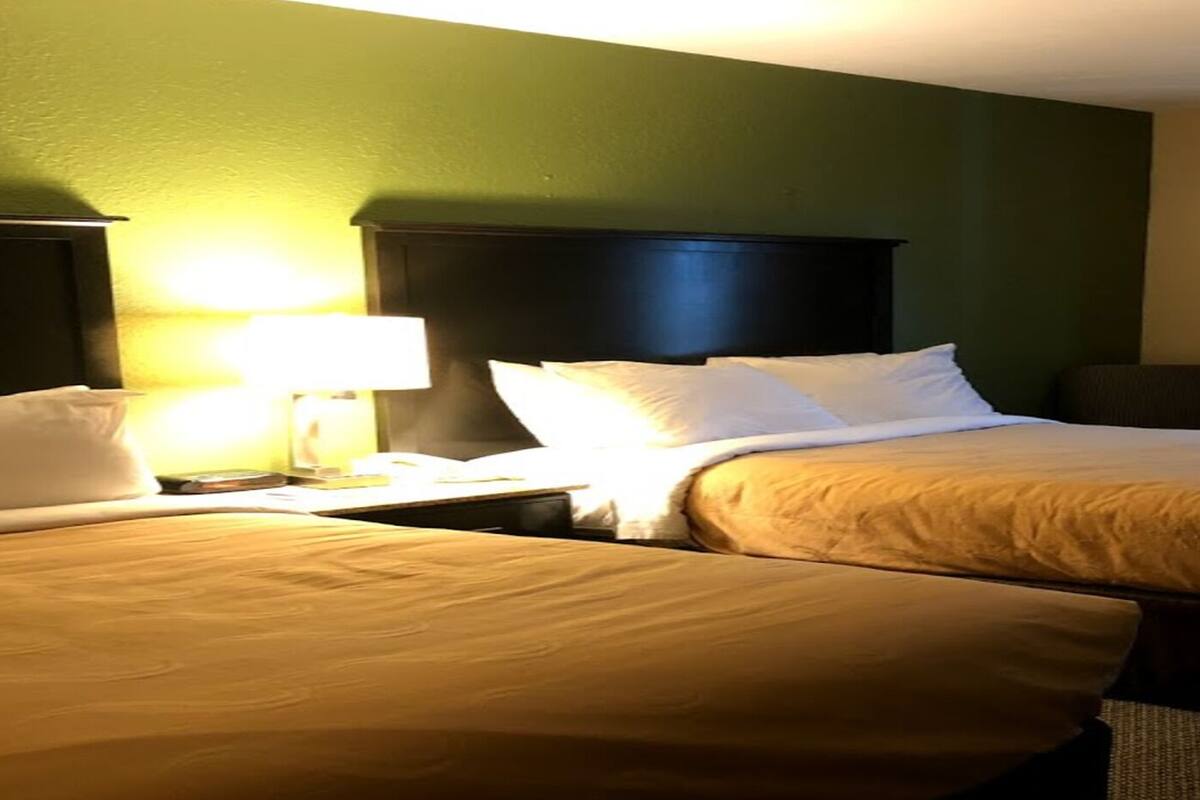 Habitación de hotel con dos camas, un escritorio, una silla, una lámpara y una ventana con cortinas.