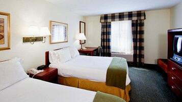 A hotel room with two beds, a desk, a television, and a window with curtains.