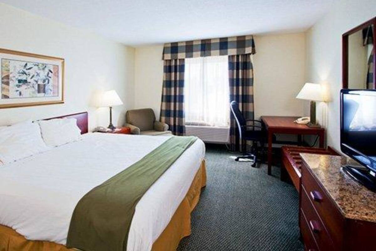Una habitación de hotel con cama, escritorio, silla, televisor y ventana con cortinas.