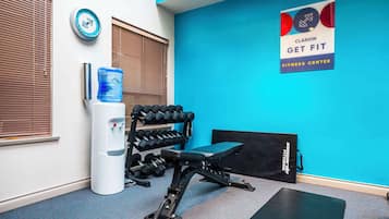Un gimnasio con pared azul, mancuernas, dispensador de agua y una banca.