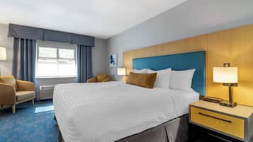 A hotel room with a large bed, a nightstand with a lamp, a chair, and a window with curtains.