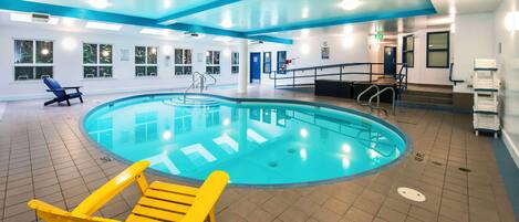 An indoor swimming pool with a blue and white color scheme, a sun lounger, and a staircase leading to an upper level.