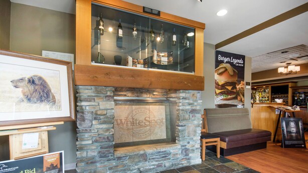 A restaurant interior with a stone fireplace, wooden bench, and a bar area. - Clarion Hotel & Conference Centre Abbotsford  (Abbotsford)