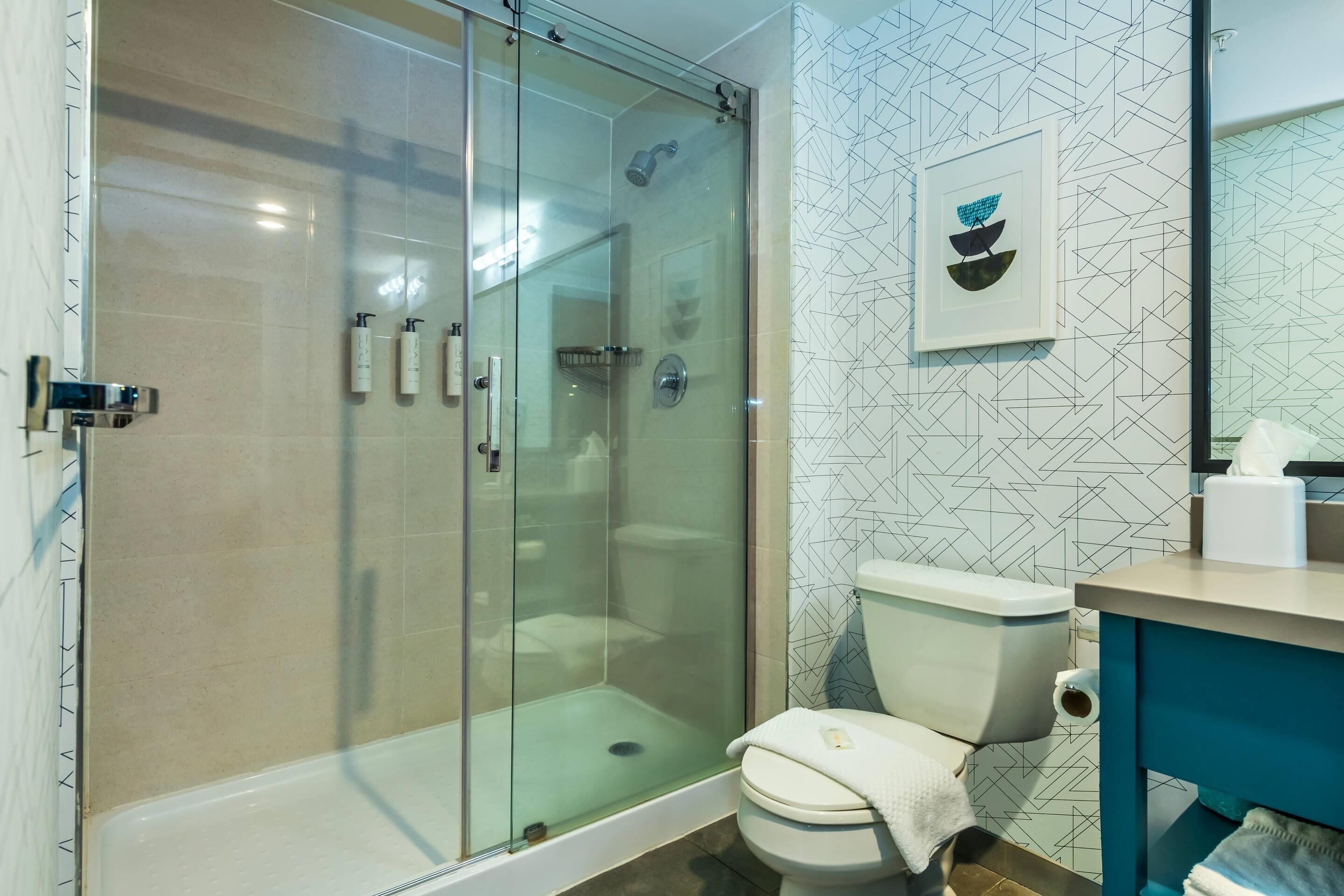 A bathroom with a glass-enclosed shower, a toilet, and a sink with a towel.