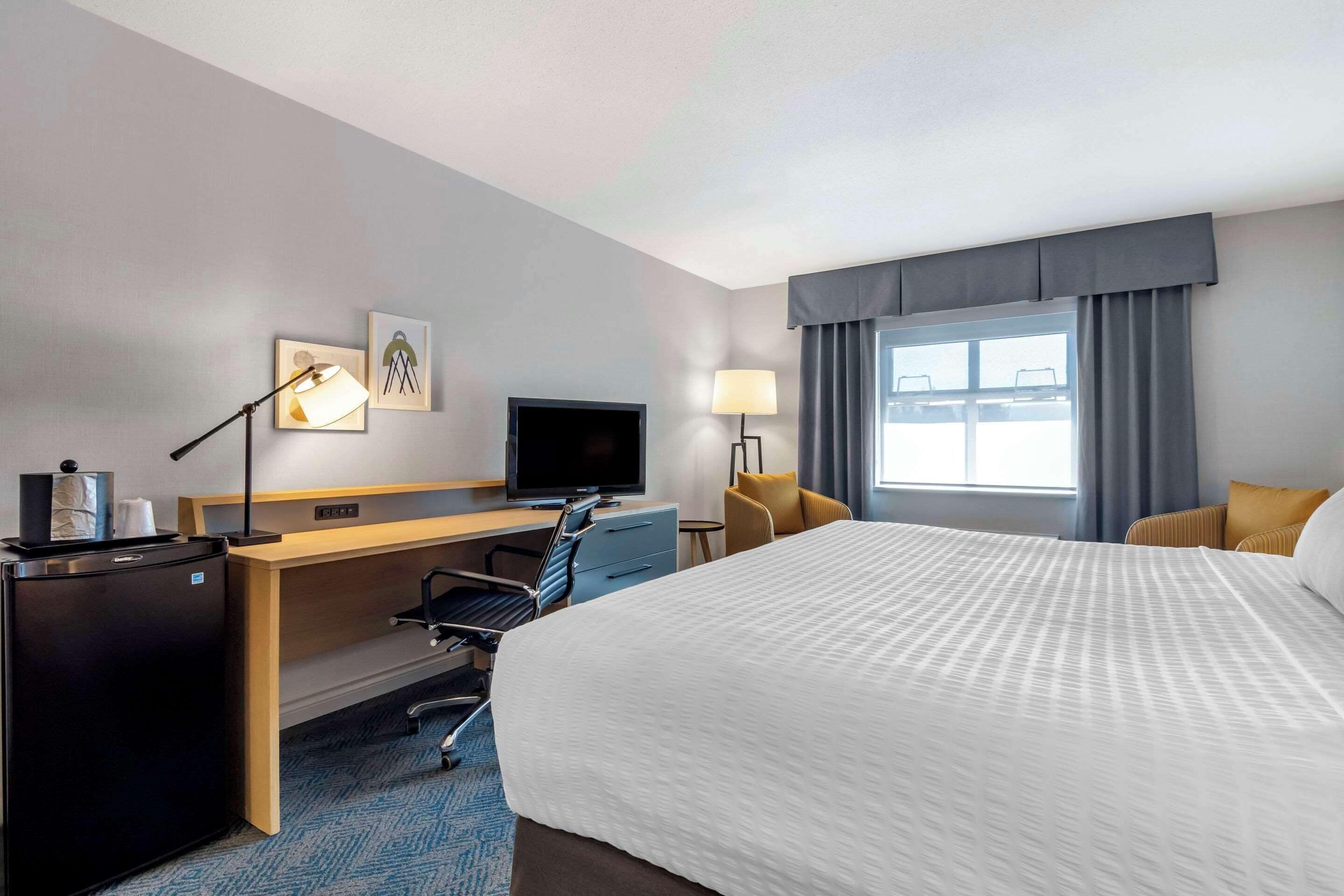 A hotel room with a bed, desk, chair, TV, and a window with curtains.
