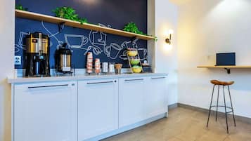 Una cuina moderna amb armaris blancs, una màquina de cafè, un bllot i una estant amb plantes i utensilis de cuina.