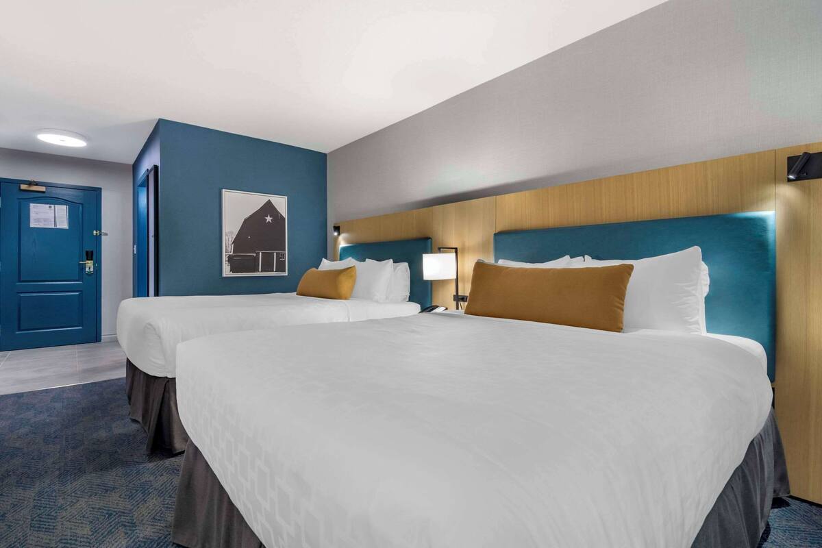 A hotel room with two beds, a wooden headboard, a blue door, and a framed picture on the wall.