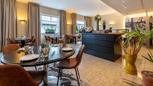 Un comedor de hotel moderno con mesas redondas, sillas de cuero marrón y una isla central con encimera negra.